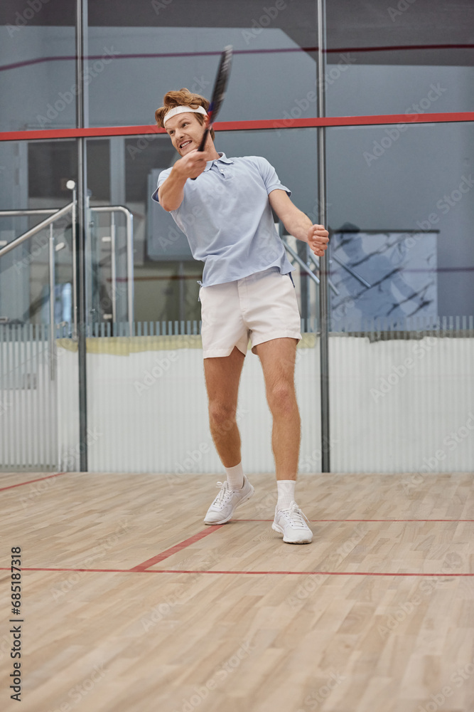 happy redhead man in headband bending over squash ball on floor inside of court, interracial friends happy redhead man in headband bending over squash ball on floor inside of court, interracial friends