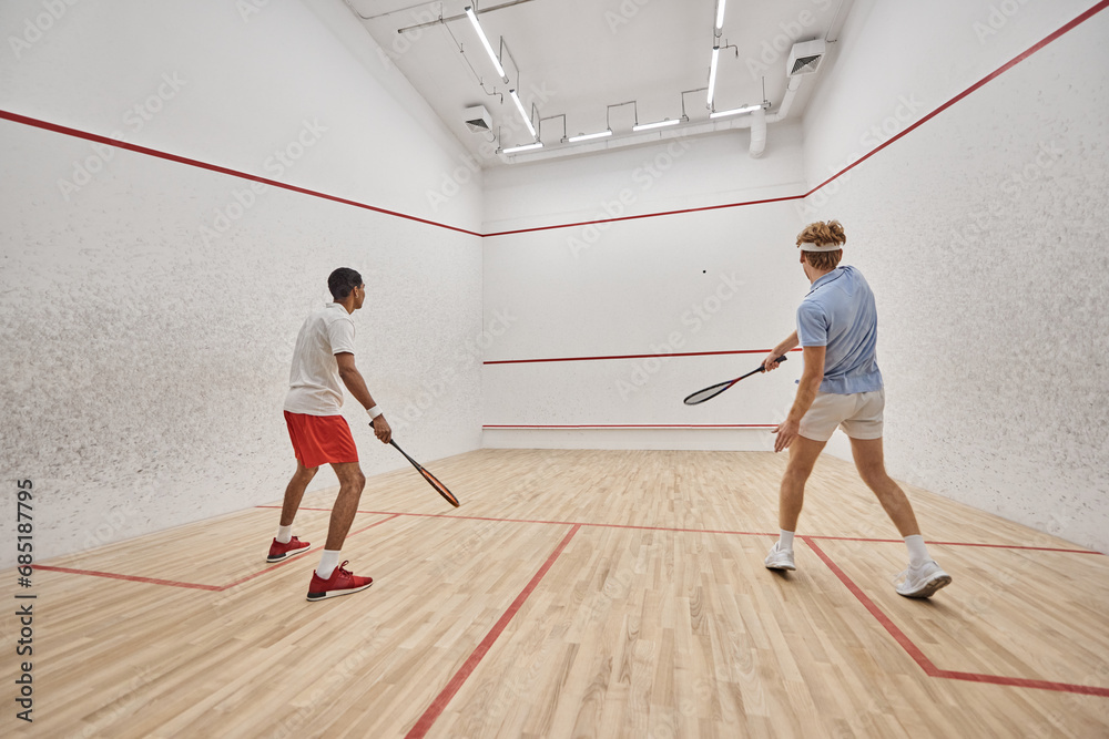 dynamic and interracial friends playing squash together inside of court, preparing for competition