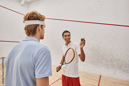 happy african american man with squash ball and racquet standing near friend inside of court © LIGHTFIELD STUDIOS