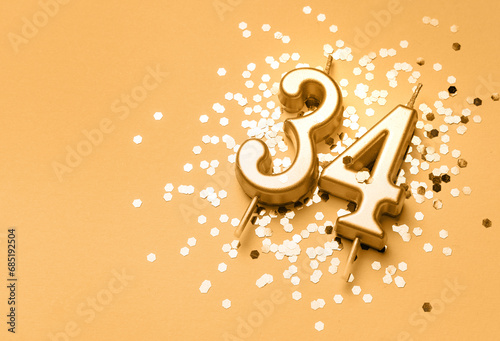 34 years birthday celebration festive background made with golden candle in the form of number Thirty four lying on sparkles. Universal holiday banner with copy space. photo