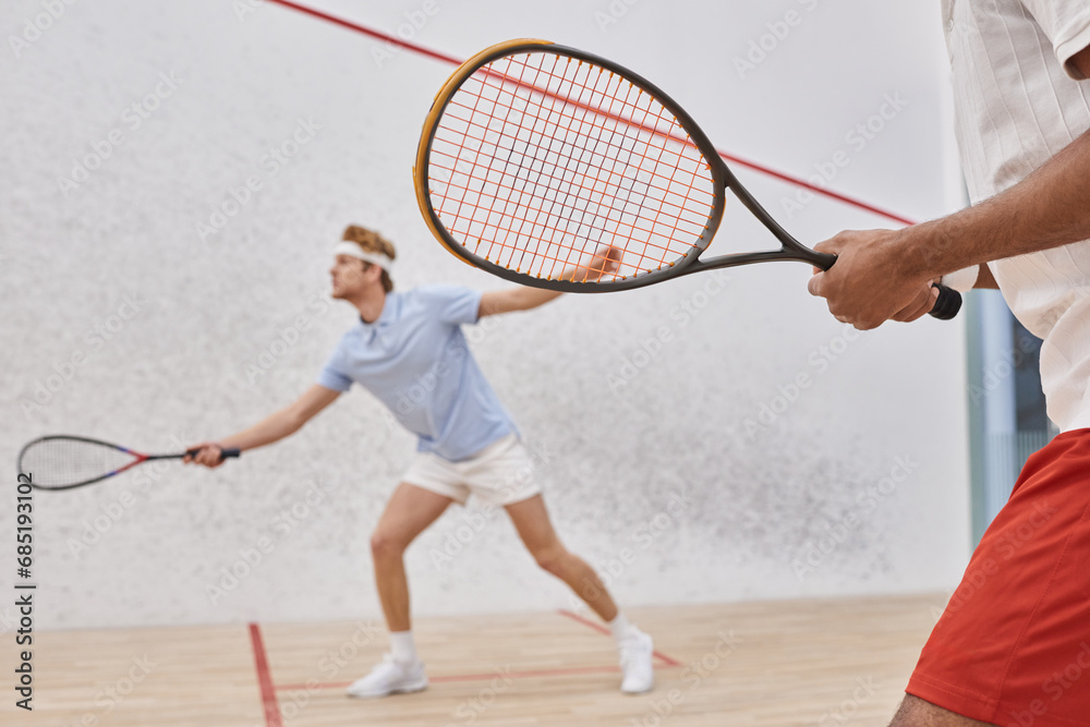 focus on african american man in sportswear playing with redhead friend inside of squash court