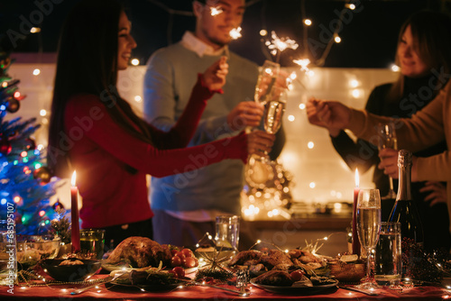 Night shot of people toasting with champagne and holding sparklers while having New Year party 