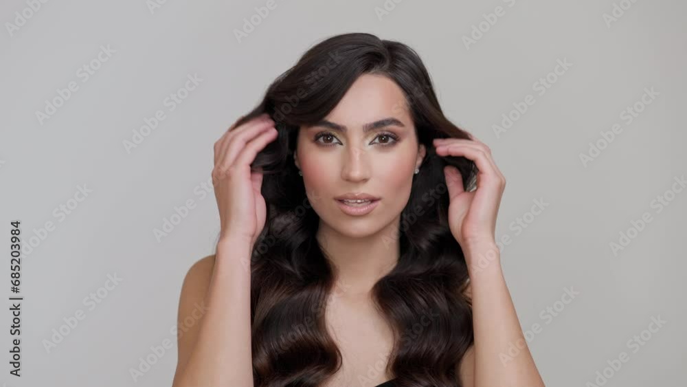 Young charming brunette with long wavy hair posing on a light gray background. Young charming brunette with long wavy hair posing on a light gray background.