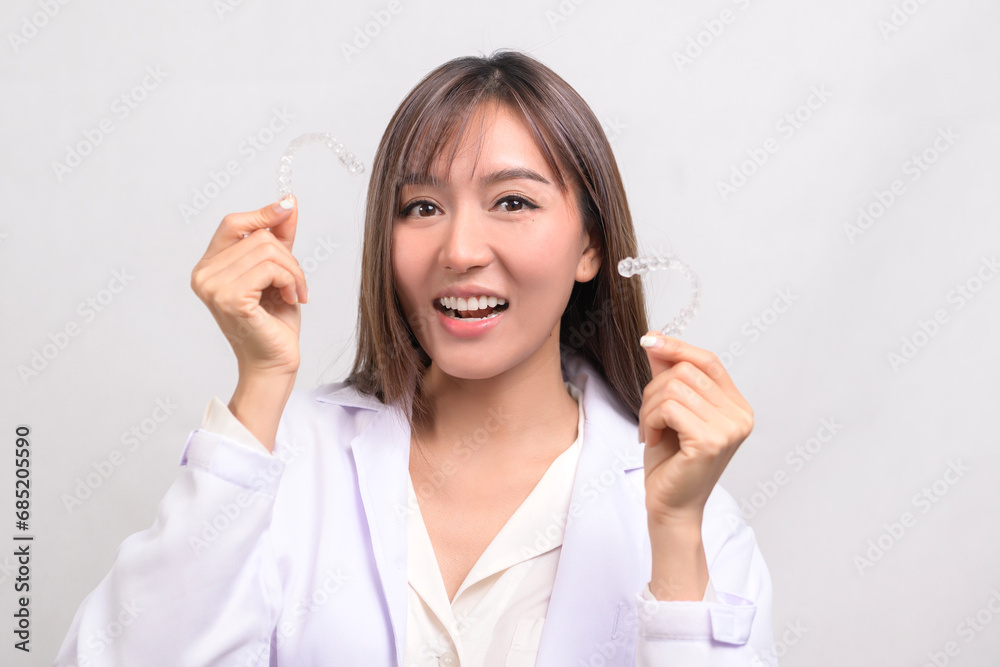 Young female dentist holding invisalign braces over white background studio, dental healthcare and Orthodontic concept. Young female dentist holding invisalign braces over white background studio, dental healthcare and Orthodontic concept.