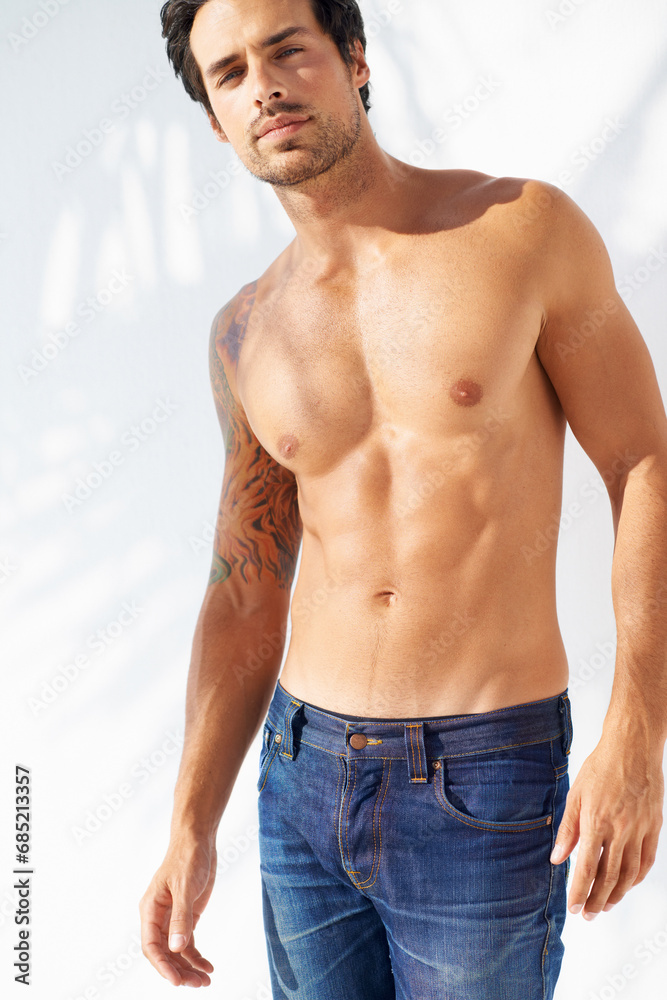 Fototapeta premium Portrait, fashion and body with a young man outdoor on a white background for masculine style. Summer, shirtless and the muscles of a confident young model in a denim jeans for health or fitness