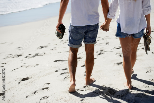Love, holding hands and couple walking on beach for date, outdoor bonding and tropical holiday. Romance, man and woman from back, legs and relax on vacation together with travel, care and adventure.