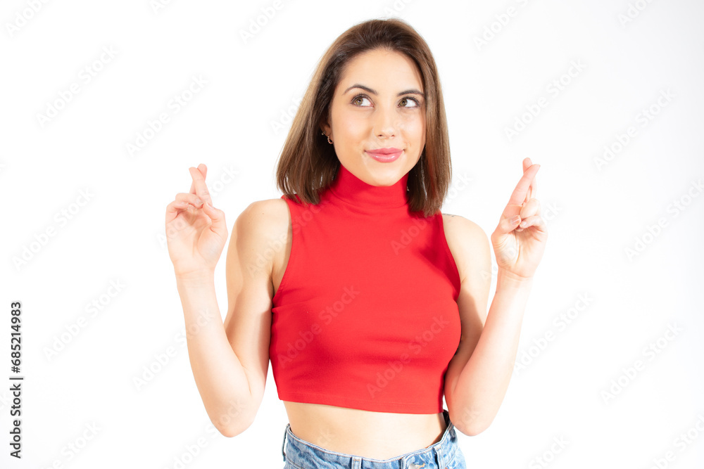 Portrait of a smiling young woman standing over white background, holding fingers crossed for good luck Portrait of a smiling young woman standing over white background, holding fingers crossed for good luck