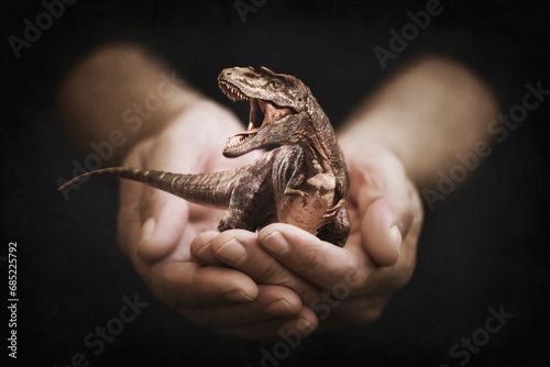Close-up of a person's hands holding a miniature roaring tyrannosaurus rex dinosaur photo