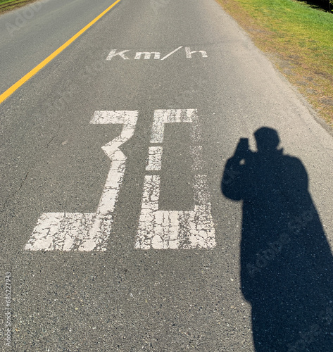 Silhouette of a man standing in a road taking a photo of a 30 km/hr speed limit road marking, British Columbia, Canada photo