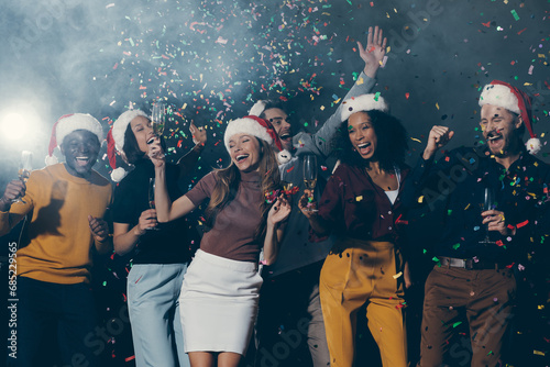 People in Christmas hats dancing and throwing confetti while celebrating New Year in night club