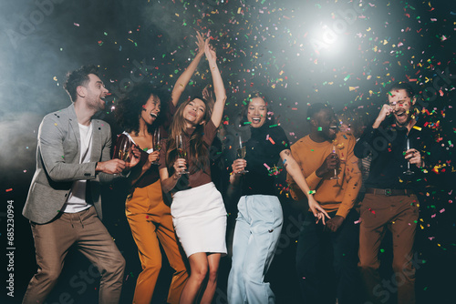 Group of young happy people enjoying champagne and throwing confetti while dancing in night club