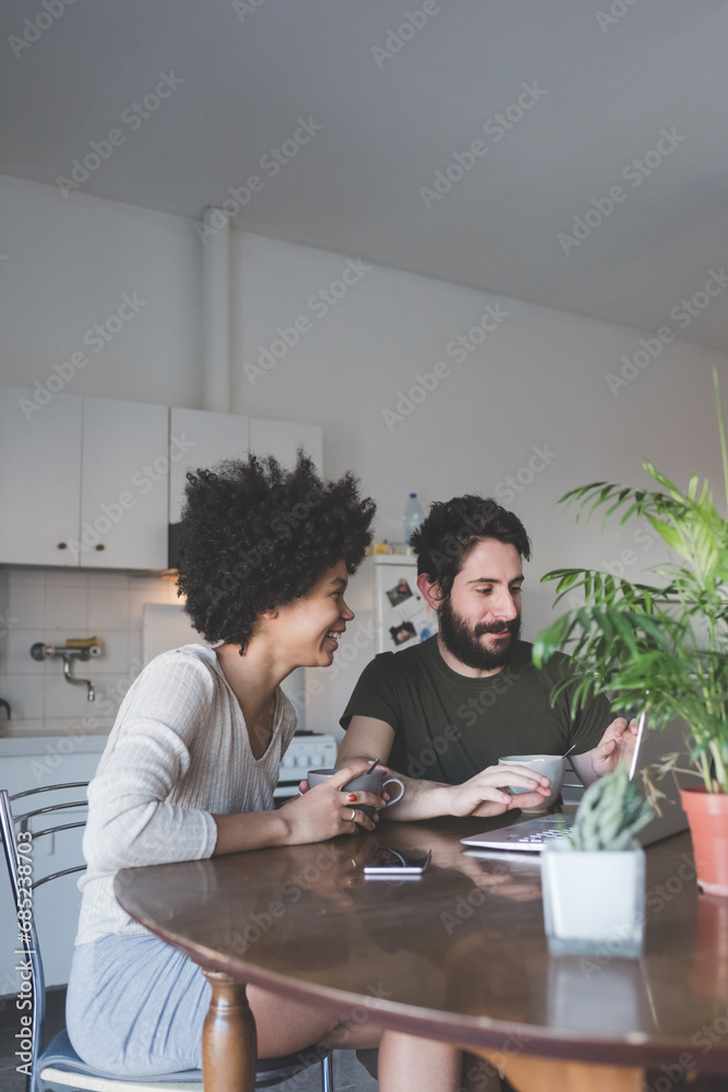 Obraz premium young multiethnic couple indoor watching streaming on computer having coffee
