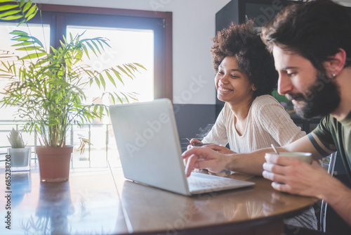 young multiethnic couple indoor watching streaming on computer having coffee photo