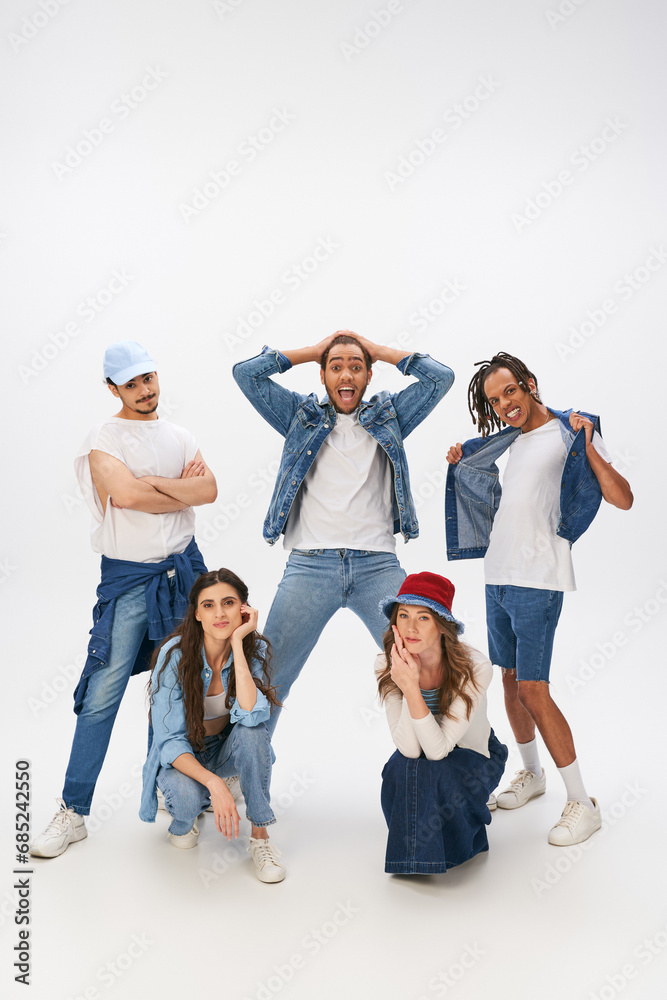 excited multicultural men posing near stylish women squatting on grey backdrop, street style