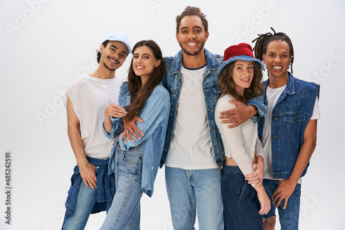 joyful african american man embracing trendy multicultural friends and looking at camera on grey