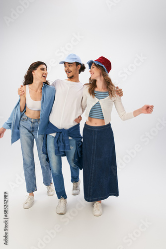full length of cheerful man and women in fashionable street wear walking together on grey backdrop