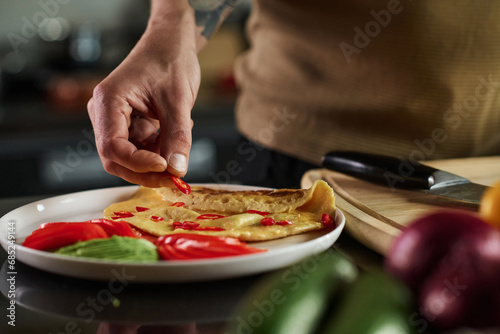 Fototapeta Naklejka Na Ścianę i Meble -  Closeup of hand of unrecognizable man placing slice of chili pepper on omelet