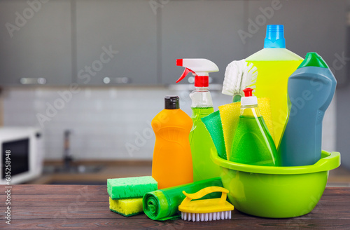 Cleaning products on a wooden table on a blurred kitchen background. Cleaning service concept. Household chemicals.Cleaning and detergents in plastic bottles, sponges and gloves.Mockup. Design. 