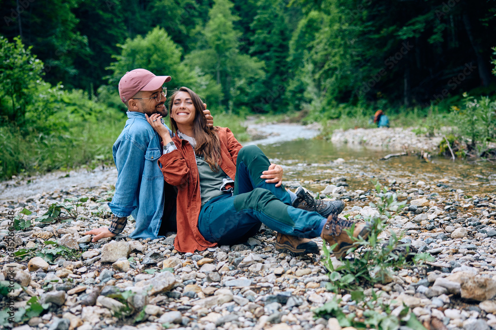 Young happy couple relaxing by creek while hiking in nature.