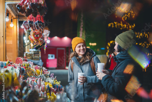 Two happy young women friends with mulled wine stands walking at a Christmas market in a European city