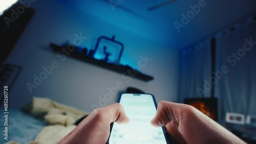 Wide pov shot person typing on smartphone touchscreen laying in bed at night photo