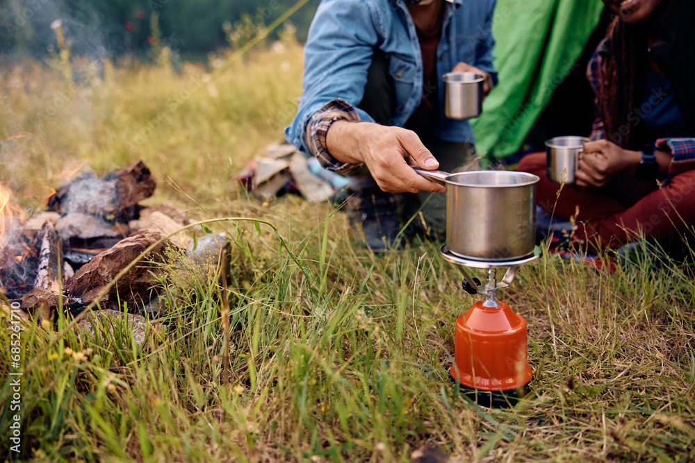 Close up of couple using portable camping stove while relaxing by their tent in nature. Close up of couple using portable camping stove while relaxing by their tent in nature.