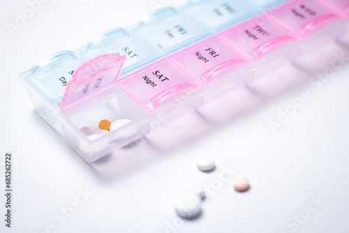Tablets and pills in plastic box on white background. Focus on foreground, soft bokeh.