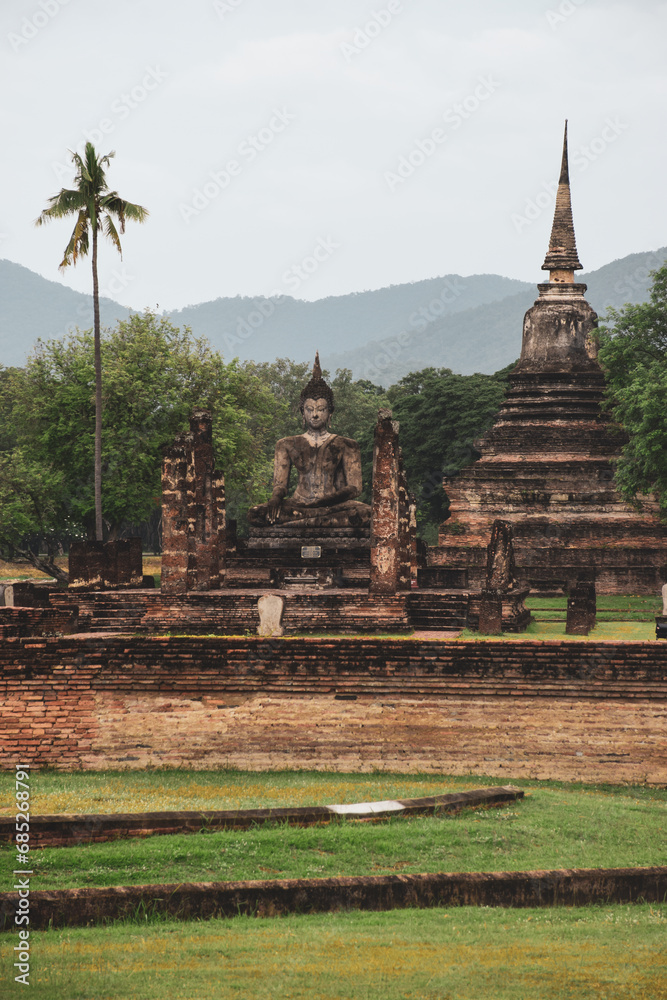 Fototapeta premium Buddhist temple surrounded by the jungle in the historical archaeological site of Sukothai in the morning light.