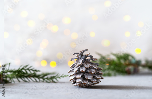 Fir cone with evergreen tree branches over grey background with blurred lights behind. Copy space for text