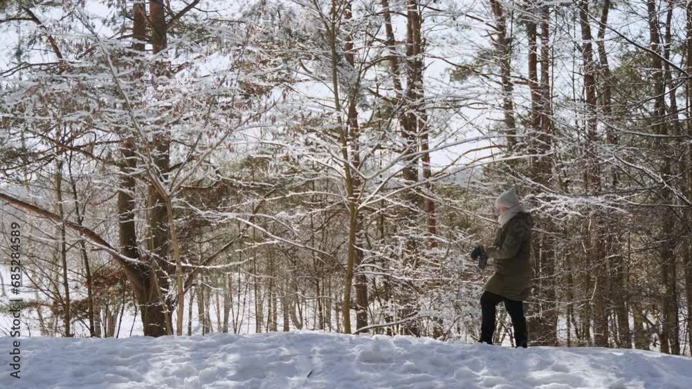 White european woman in warm clothes walks along edge of winter forest and puts on mittens. Frosty sunny morning and healthy walk in park. Pensive traveler during tourist route. White european woman in warm clothes walks along edge of winter forest and puts on mittens. Frosty sunny morning and healthy walk in park. Pensive traveler during tourist route.