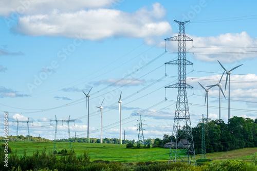 An industrial nature landscape with many high voltage power lines pylons and wind generators
