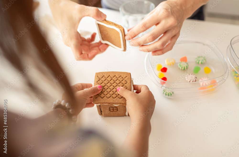 Obraz premium Mother and child putting together a gingerbread house, family Christmas activities 