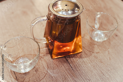 Glass Teapot with Hot Tea and Two Transparent Cups on Cafe Table photo