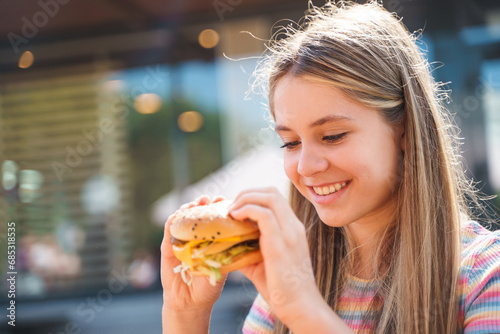Teenage girl eating a burger at the outside restaurant
