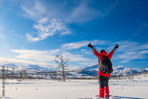 Sporty person in red sport jacket enjoys snow and breathtaking Norwegian landscape. Sunny winter activity.