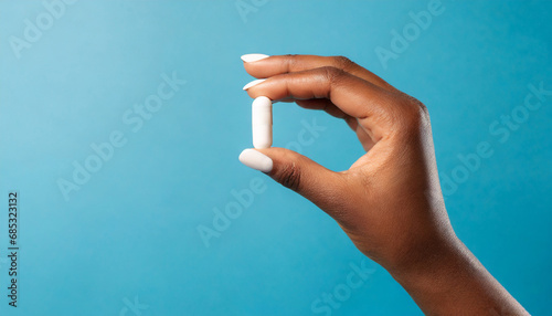 female hand holding white capsule on blue background close copy space pharmacology concept