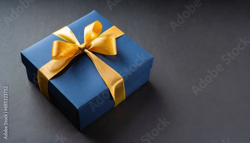 dark blue gift box with gold satin ribbon on dark background top view of birthday gift with copy space for holiday or christmas present