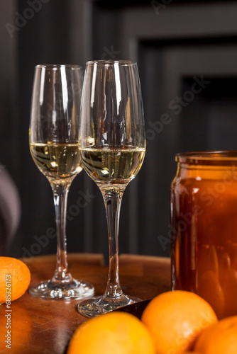 Fotografie Two glasses of champagne and tangerines on a table against blurred black background