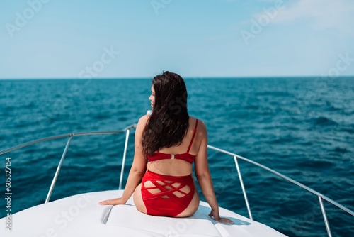 Yacht woman in a red bikini posing while on the bow of a yacht. Happy woman is sunbathing on the bow of a ship during a boat trip. Travel concept, vacation at sea © svetograph