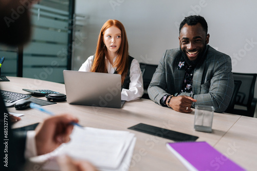 Process in boardroom between multiethnic positive business partners. Diverse businesspeople gathered in office talking solving issues, working on project, share thoughts during meeting.