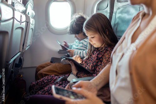 Little boy and girl sitting on airplane using tablet photo