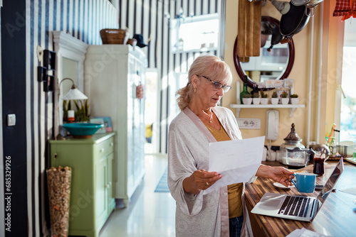 Senior woman standing holding document at home