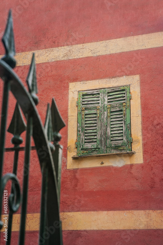 window with green, old, peeling shutters and fragment of a forged fence on an...