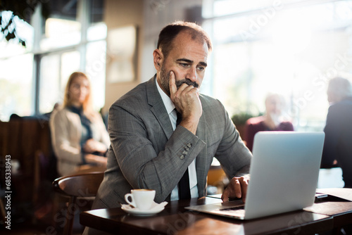 Middle aged man in formal suit using laptop in cafe or bar photo