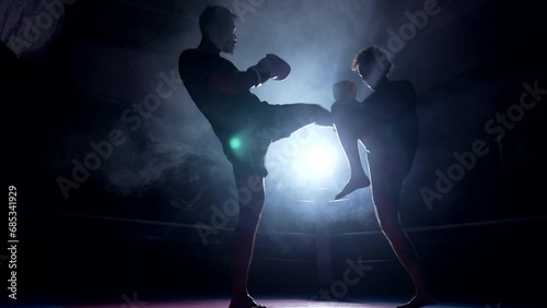 Two fighters battling each other inside boxing ring with dramatic backlight. Opponents kicking and punching each other in intense fight training photo