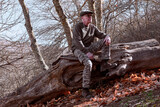 hombre adulto sentado en un viejo castaño caído al suelo con ambiente otoñal