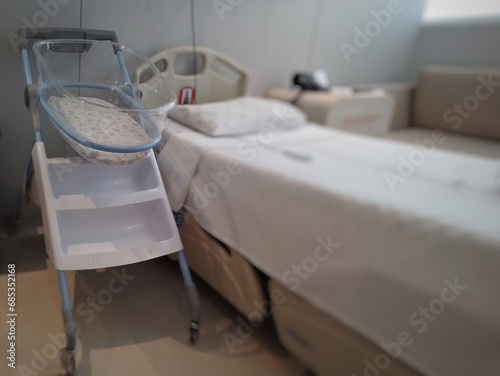 Acrylic crib for newborn, next to the bed in a maternity room.