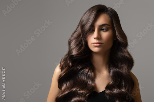 Beautiful young woman with wavy long hair. Portrait on a gray background