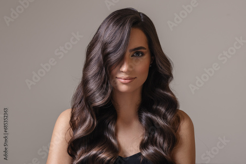 Beautiful young woman with wavy long hair. Portrait on a gray background