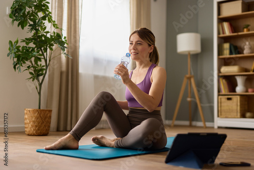 Woman drinking water while practicing yoga at home